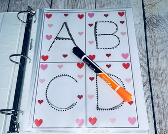 Op de afbeelding: Een wit vel papier met de letters A, B, C en D die zijn omlijnd met zwarte stippen. De letters zijn in een 2x2 raster gerangschikt. Er zijn roze hartjes rond de letters verspreid. Een zwarte stift en een oranje stift liggen op het papier.