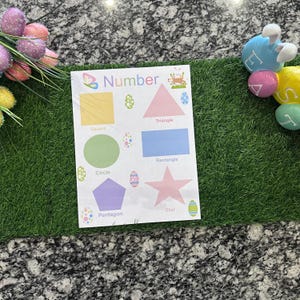 May include: A white educational poster with the word "Number" and various shapes in different colors. The shapes include a yellow square, pink triangle, blue rectangle, green circle, purple pentagon, and pink star. Easter egg decorations are also present.