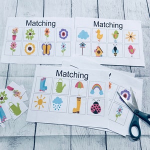 May include: A set of spring-themed matching cards with images of flowers, a butterfly, a bird, a bee, a house, a watering can, a rain cloud, a rainbow, a ladybug, a sun, a pair of rain boots, and an umbrella. The cards are printed on white paper with black text that reads "Matching".