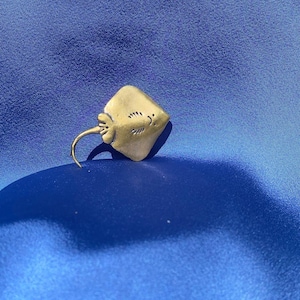 May include: A gold-coloured metal stingray figurine with a smiling face. The figurine is on a blue background.