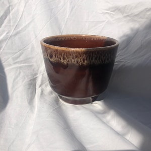 May include: A brown ceramic planter with a white glaze. The planter has a rounded shape and a slightly flared lip.