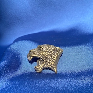 May include: A gold-colored metal bottle opener shaped like a roaring jaguar's head.