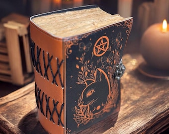 May include: A brown leather-bound journal with a black cover featuring a pen and ink illustration of a cat, flowers, and a pentagram. The journal has decorative stitching and a metal clasp.