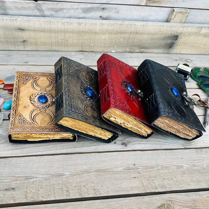 Op de afbeelding: Vier lederen dagboeken met decoratieve maan- en stermotieven. Elk dagboek heeft een sluiting van blauwe edelsteen en verouderde papierpagina's.