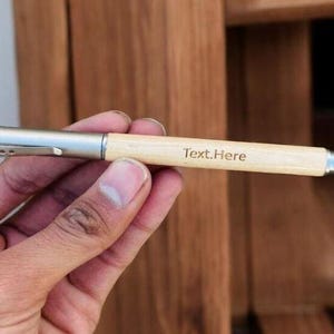 May include: A wooden pen with a silver metal clip and a silver metal end. The pen is engraved with the text "Text.Here".