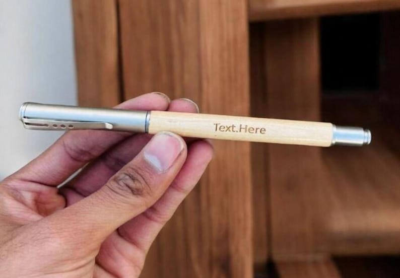 May include: A wooden pen with a silver metal clip and a silver metal end. The pen is engraved with the text "Text.Here".