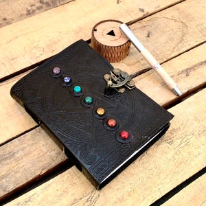 May include: A black leather journal with a decorative embossed design and a metal clasp. The journal has a row of colorful gemstones around the edge.