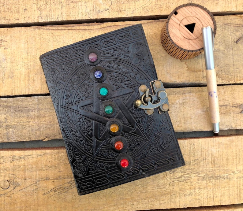 May include: Black leather journal with a pentacle design and a brass lock. The journal has seven colorful gemstones embedded in the pentacle design.