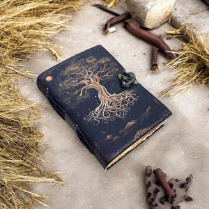 May include: A black leather journal with a gold tree design and a metal clasp. The journal has a distressed look and is perfect for writing down your thoughts and ideas.