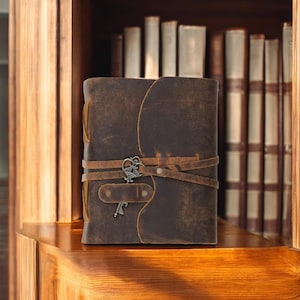 Pode incluir: Um di&aacute;rio de couro marrom com um chaveiro e v&aacute;rias tiras. O di&aacute;rio est&aacute; sentado em uma prateleira de madeira na frente de uma estante de livros.