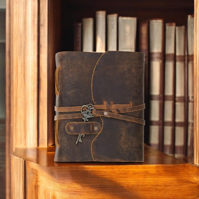 Pode incluir: Um di&aacute;rio de couro marrom com um chaveiro e v&aacute;rias tiras. O di&aacute;rio est&aacute; sentado em uma prateleira de madeira na frente de uma estante de livros.