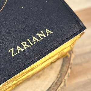 May include: A black leather journal with gold stitching and the word "Zariana" embossed in gold on the cover.
