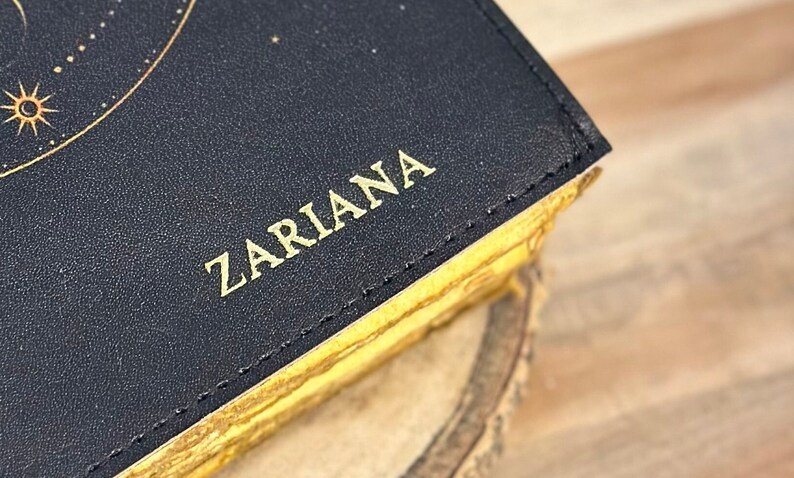 May include: A black leather journal with gold stitching and the word "Zariana" embossed in gold on the cover.