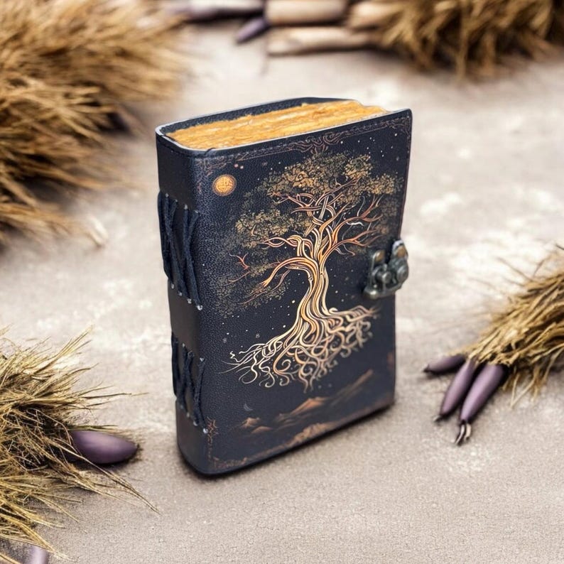 May include: A black leather journal with a gold tree design and a metal clasp. The journal is closed and has a rustic look.