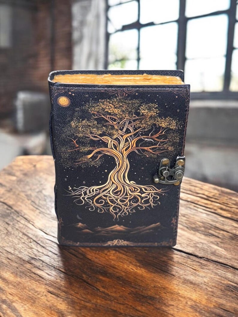 May include: A black leather journal with a gold tree of life design. The journal has a clasp closure and a decorative border.