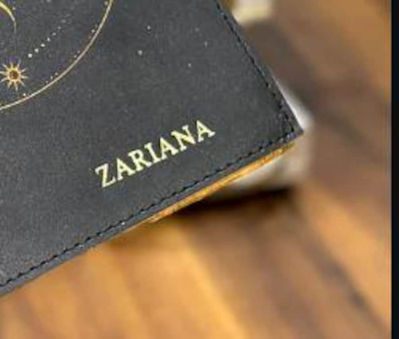 May include: Close-up of a black leather wallet with gold lettering that reads "ZARIARA".