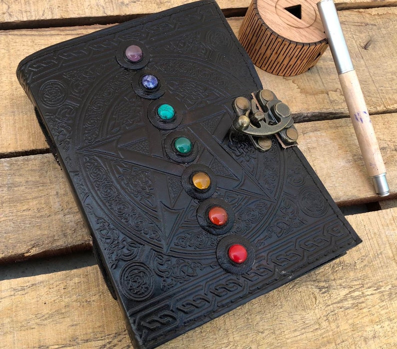 May include: Black leather journal with a pentagram design and colorful gemstones around the edges. The journal has a brass lock and clasp.