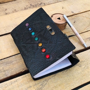May include: Black leather journal with a pentagon design and a lock. The journal is decorated with colorful gemstones around the pentagon.