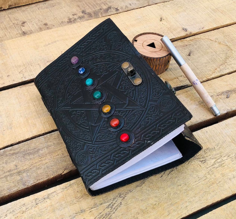 May include: Black leather journal with a pentagon design and a lock. The journal is decorated with colorful gemstones around the pentagon.