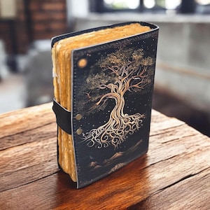 May include: A black leather journal with a gold tree design and a strap closure. The journal has a rustic look and is perfect for writing down thoughts and ideas.