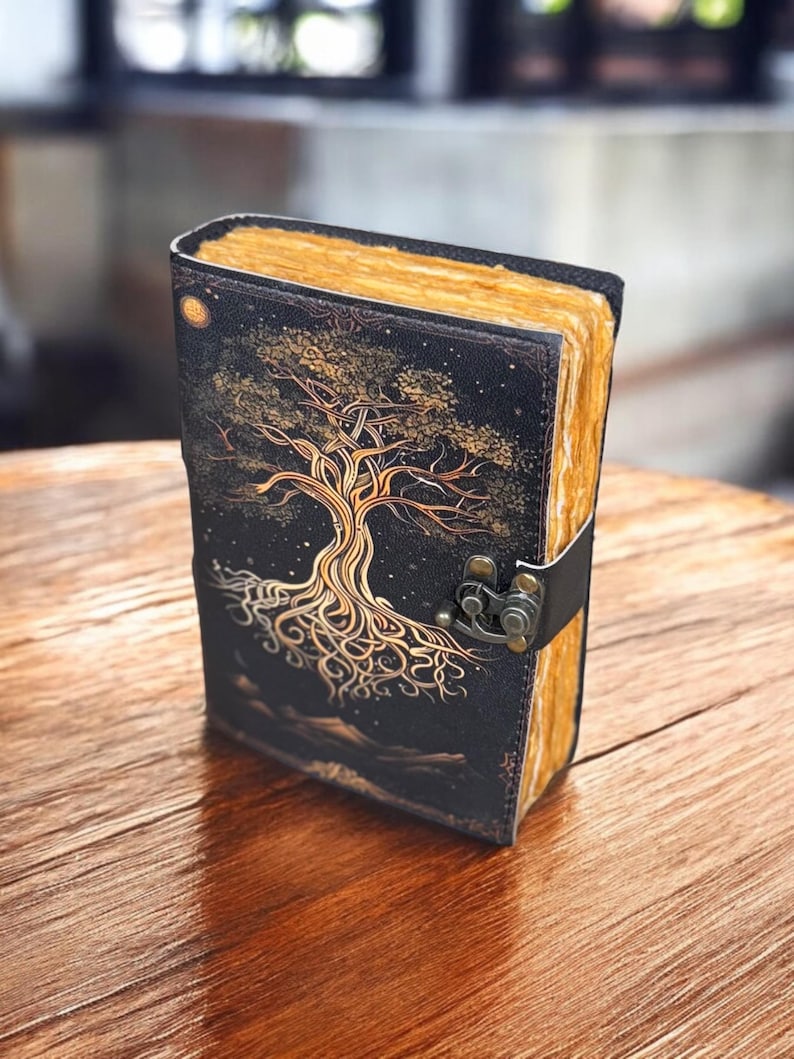 May include: A black leather journal with a gold tree design and a clasp closure. The journal has a distressed look and is perfect for writing or sketching.