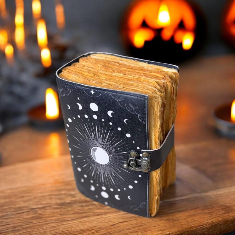 May include: A black leather-bound journal with a moon and stars design. The journal has a clasp closure and is open to reveal aged pages.