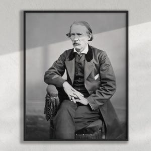 May include: Black and white framed portrait of a seated man. The man wears a dark suit with a vest, a white collared shirt, and a dark tie. He has a mustache and is seated in a chair with decorative armrests.