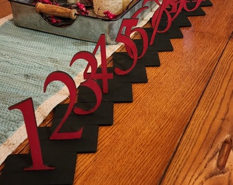 Könnte beinhalten: Rote Holznummern von 1 bis 10 auf schwarzen quadratischen Sockeln, diagonal auf einem Holztisch angeordnet.