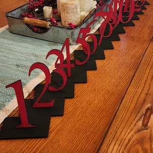 May include: Red wooden numbers 1 to 10 on black square bases, arranged in a diagonal line on a wooden table.