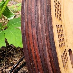 K&ouml;nnte beinhalten: Nahaufnahme eines Holzspielbretts mit einem dunkelbraun gebeizten Rand. Das Brett hat eine Reihe von L&ouml;chern in einem kreisf&ouml;rmigen Muster.