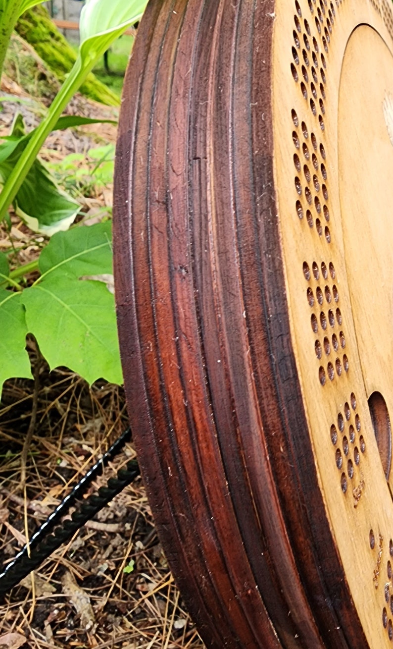 K&ouml;nnte beinhalten: Nahaufnahme eines Holzspielbretts mit einem dunkelbraun gebeizten Rand. Das Brett hat eine Reihe von L&ouml;chern in einem kreisf&ouml;rmigen Muster.