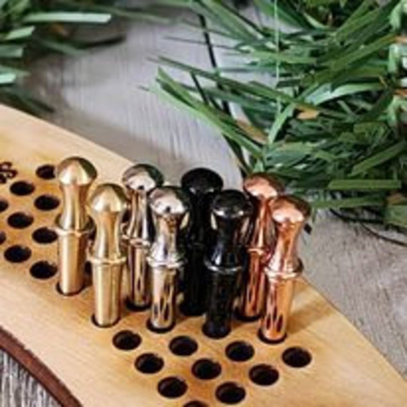 K&ouml;nnte beinhalten: Ein Holzspielbrett mit einem Gitter aus L&ouml;chern und Metallpf&auml;hlen in verschiedenen Farben, darunter Gold, Silber und Schwarz. Die Pf&auml;hle sind in einer Reihe &uuml;ber das Brett angeordnet.