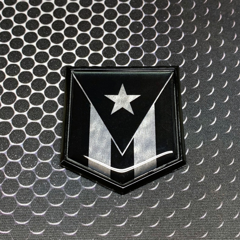 K&ouml;nnte beinhalten: Ein schwarzes und silbernes schildf&ouml;rmiges Emblem mit einem wei&szlig;en Stern und drei silbernen Streifen. Das Emblem befindet sich auf einem schwarz-wei&szlig;en gemusterten Hintergrund.