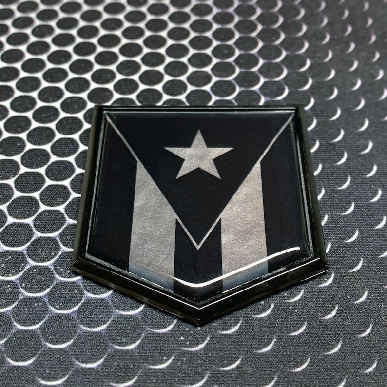 K&ouml;nnte beinhalten: Ein schwarzes und silbernes schildf&ouml;rmiges Emblem mit einem wei&szlig;en Stern und drei Streifen. Das Emblem ist aus gl&auml;nzendem Material gefertigt und hat einen schwarzen Rand.