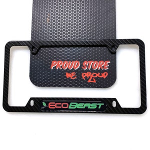 May include: Black carbon fiber license plate frame with a green leaf and the text "ECO BEAST" in white. The frame is on top of a black background with the text "PROUD STORE BE PROUD" in red.
