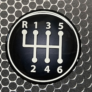 May include: Black and white gear shift pattern sticker with the letters R, 1, 2, 3, 4, 5, and 6.