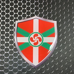 May include: A red, white, and green shield-shaped sticker with a stylized green and red symbol in the center. The sticker is on a black and white background.