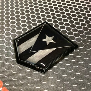 K&ouml;nnte beinhalten: Ein sechseckiger Aufkleber in Schwarz und Silber mit der Flagge von Puerto Rico. Die Flagge zeigt einen wei&szlig;en Stern auf einem roten Dreieck mit drei wei&szlig;en Streifen.