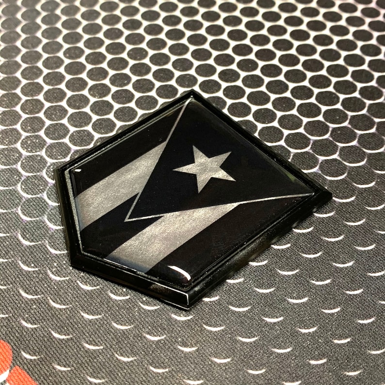 K&ouml;nnte beinhalten: Ein sechseckiger Aufkleber in Schwarz und Silber mit der Flagge von Puerto Rico. Die Flagge zeigt einen wei&szlig;en Stern auf einem roten Dreieck mit drei wei&szlig;en Streifen.
