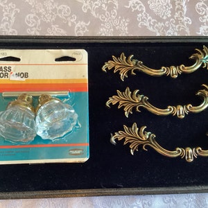 May include: A pack of two glass door knobs with gold trim and a set of three ornate gold door pulls. The pack is labelled "Glass Door Knob" and the number "55-0183".