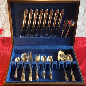 Puede incluir: Una caja de madera con un interior de terciopelo azul que contiene un juego de cubiertos de plata. Los cubiertos incluyen cuchillos, tenedores, cucharas y piezas para servir. La caja está abierta y los cubiertos están dispuestos en el forro de terciopelo.