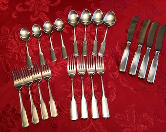 Op de afbeelding: Een set roestvrijstalen bestek bestaande uit vier dinermessen met afgeronde punten, acht lepels van verschillende groottes en acht vorken. Elk stuk heeft een eenvoudig, glad handvatontwerp met een gepolijste metalen afwerking.