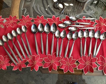 Puede incluir: Un juego de 20 cucharas de plata con mangos adornados dispuestos sobre un mantel floral rojo y dorado.