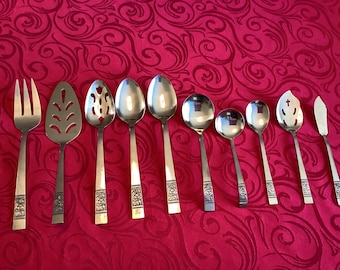 Op de afbeelding: Een set van tien roestvrijstalen bestekdelen, waaronder een serveervork, een taartschep met sleuven, twee grote lepels, een dinerlepel, twee kleinere lepels, een kleine lepel met sleuven en een botermes, alle met een bloemmotief op de steel.