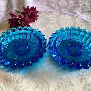 Puede incluir: Dos candelabros de vidrio azul turquesa con borde de cuentas y un anillo central para una vela.