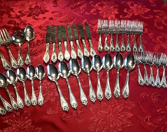 May include: A set of silverware laid out on a red tablecloth. The set includes forks, knives, and spoons. The silverware is made of polished silver and has an ornate design.