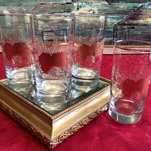 May include: Four clear glass tumblers with gold rims and a red and white design. The glasses are on a gold mirrored tray with a gold frame.
