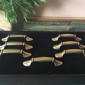 May include: Set of eight antique gold cabinet drawer pulls with a decorative design. The pulls are arranged in a display box with black velvet lining.