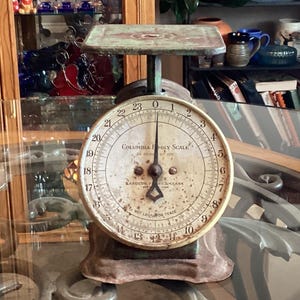 Puede incluir: Una antigua báscula familiar Columbia con un dial circular y una pequeña plataforma. El dial muestra números del 0 al 24. La báscula tiene un aspecto vintage y desgastado, con una combinación de colores verde y marrón. El texto "COLUMBIA FAMILY SCALE" es visible.