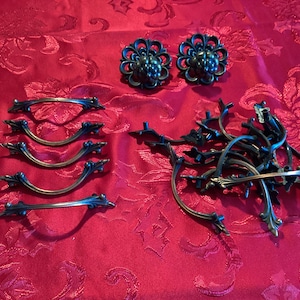 May include: A collection of antique-style cabinet hardware, including 12 ornate drawer pulls and two decorative knobs. The hardware is made of a dark metal with a distressed finish.